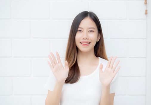 Beautiful young asian woman confident gesture say hello or greeting with waving her hand on cement background at home, friendly welcome, portrait girl cheerful expression happy and satisfied.