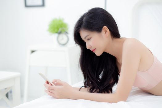 Beautiful young asian woman sexy in underwear chatting on mobile phone in the bedroom, happy girl in lingerie looking social media on smartphone lying on bed, communication and lifestyle concept.