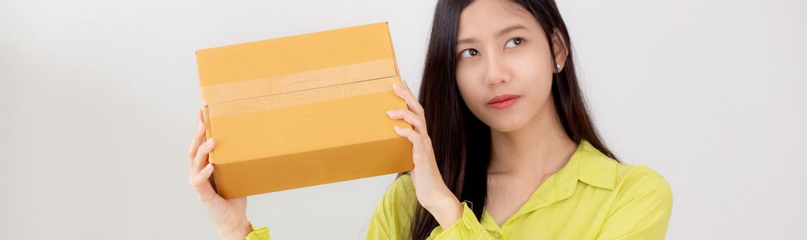 Young asian woman smiling and holding cardboard box with surprise at home, happy female carrying parcel box with excited, present and gift, packaging for deliver, online shopping store and service concept.