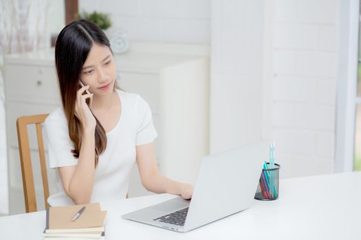 Young asian woman talking phone and work from home with laptop computer, freelance using notebook to internet online and speak on smartphone, domestic life, business and communication concept.