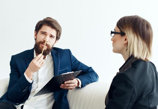 Business man with documents explains something to a young woman Sitting on a sofa indoors. High quality photo