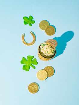 St Patrick's Day concept. Modern still life with lucky symbols and sweet food for Saint Patrick's Day party. Green velvet cupckake, shamrock, golden coins and horseshoe on blue background. Vertical