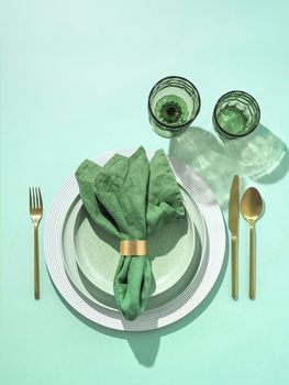 Beautiful festive table setting in green colors for St.Patrick's day with golden cutlery. Top view of Saint Patrick's day holiday table with green napkin and green glasses. Vertical. Copy space