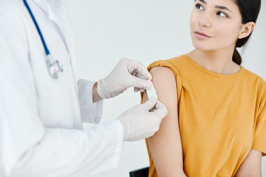 a doctor in protective gloves to stick an injection plaster on a woman in a yellow t-shirt. High quality photo