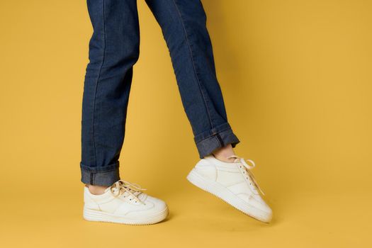 Fashionable shoes white sneakers legs yellow background cropped view. High quality photo