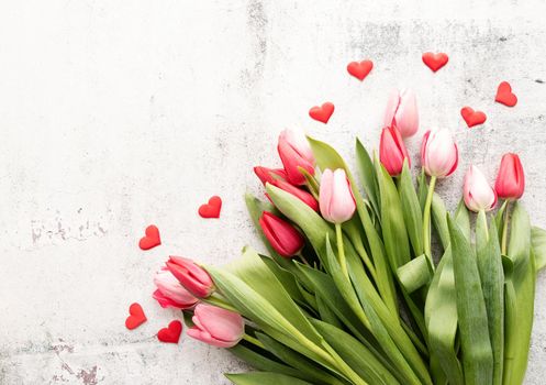 Pink and red tulips bouquet with red hearts top view on concrete background, flat lay, copy space