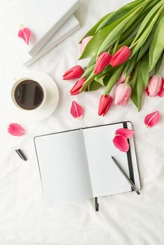 Holiday and celebration. Spring holidays. Top view of opened blank notebook with tulips and cup of coffee on white bed