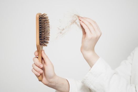 woman removes a bun of hair with a wooden comb on a light background health problems loss. High quality photo