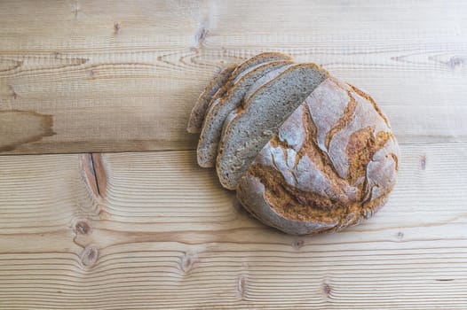 Fresh dark bread in slices, lying on a wooden cutting board.