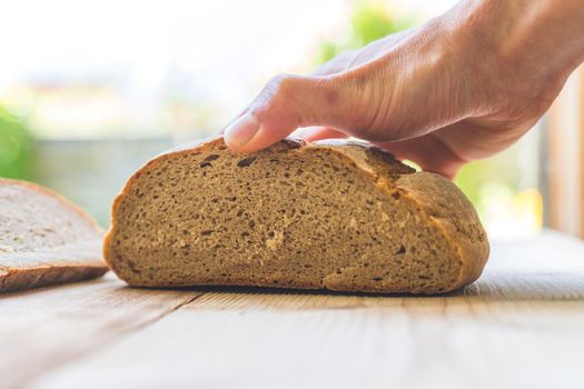 Male hand is holding a fresh rustic dark bread outdoors, breakfast
