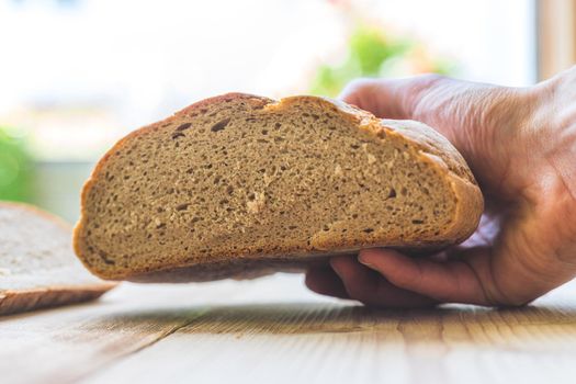 Male hand is holding a fresh rustic dark bread outdoors, breakfast