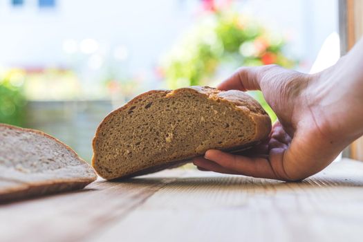 Male hand is holding a fresh rustic dark bread outdoors, breakfast