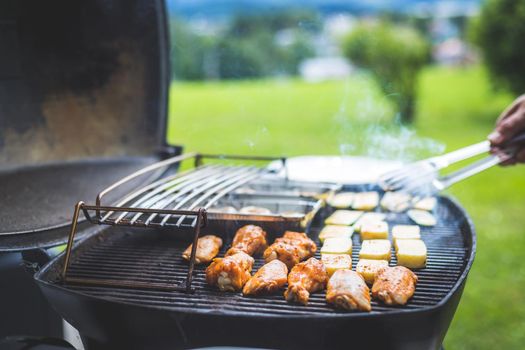 Close up of chicken wings, cheese and vegetables on gas grill. Summer time, outdoors.