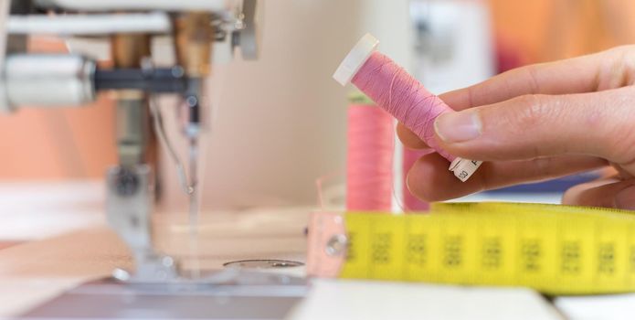 Close up of female hand holding a pink thread in a tailor workshop