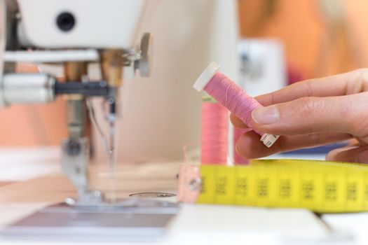 Close up of female hand holding a pink thread in a tailor workshop