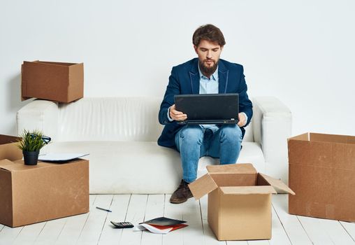 A man sits on the couch in front of a laptop working boxes with things unpacking a new office. High quality photo