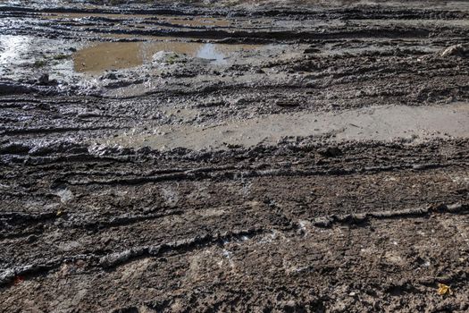 dirty wet clay mud road with tire tracks and puddles at day time - full frame background with hard sun light