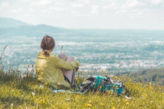 Sporty girl on a hiking trip is sitting on the meadow an enjoying the view over the far away city