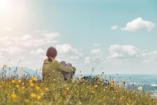 Sporty girl on a hiking trip is sitting on the meadow an enjoying the view over the far away city