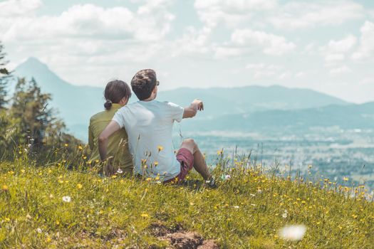 Couple on a hiking trip is sitting on the meadow an enjoying the view over the far away city