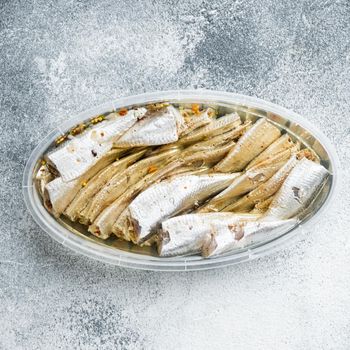 Salted anchovy fillets set, in plastic container, on gray background, top view flat lay, square format