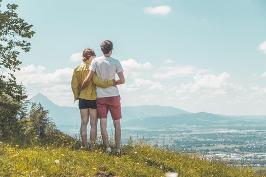 Couple on a hiking trip is standing on the meadow an enjoying the view over the far away city