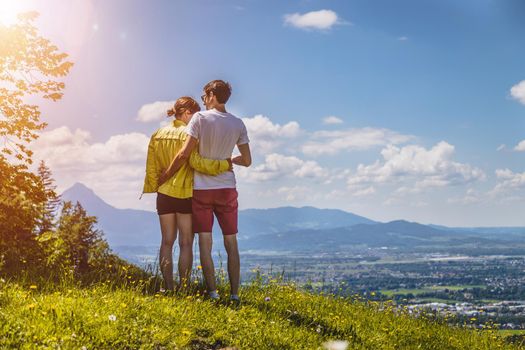 Couple on a hiking trip is standing on the meadow an enjoying the view over the far away city