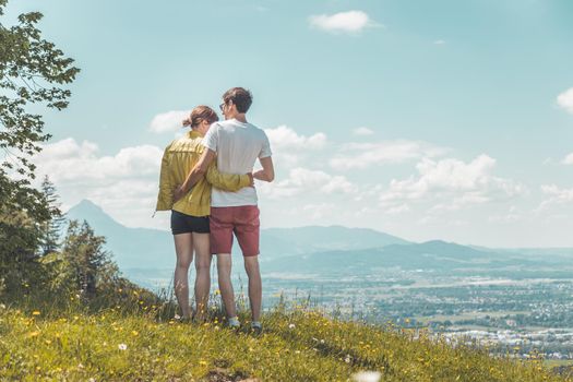 Couple on a hiking trip is standing on the meadow an enjoying the view over the far away city