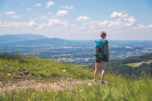 Sporty girl on a hiking trip is standing on the meadow an enjoying the view over the far away city