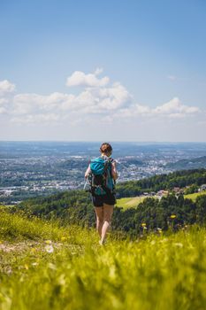 Sporty girl on a hiking trip is standing on the meadow an enjoying the view over the far away city