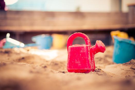 Children plastic toys in the sand box. Watering can, selective focus.