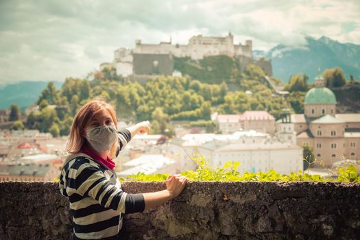 Female tourist with face mask is enjoying the view over the historic district of Salzburg