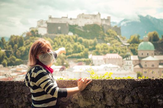 Female tourist with face mask is enjoying the view over the historic district of Salzburg
