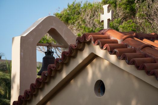 Roof of a beautiful house with a cross and a bell on it in Malia, Crete, Greece