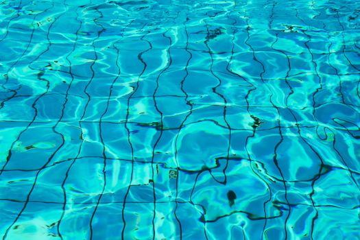 Blue and bright water in a swimming pool with sun reflection