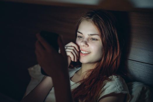 woman lies out of bed at night with a phone in her hands rest virtual room. High quality photo