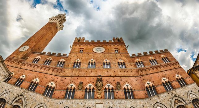 View of Palazzo Pubblico - aka Town Hall - and the Torre del Mangia medieval tower, iconic landmarks of Siena, Italy