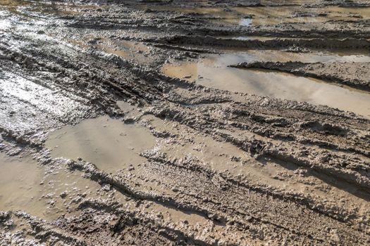 dirty wet clay mud road with tire tracks and puddles at day time - full frame background with hard sun light