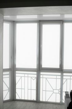 White fabric roller blinds on the plastic window on a balcony in the living room with a reflection in a stretch ceiling