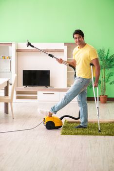 Injured man on crutches vacuum cleaning house