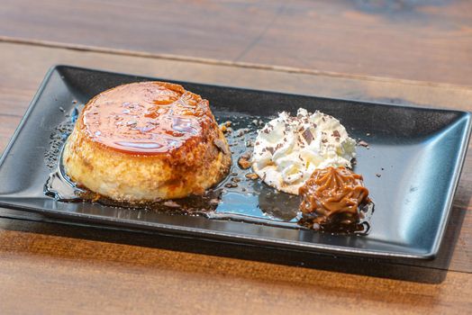 Homemade flan with cream and dulce de leche served on a black plate.