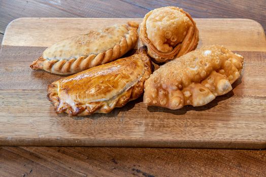Varied Argentine empanadas with different fillings on a wooden board.