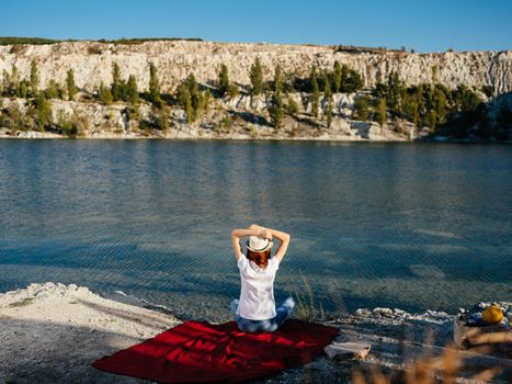 A woman sits on a red cloth near the river and gestures with her hands. High quality photo