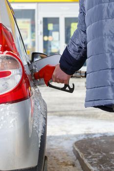 old man hand in blue warm jacket refueling gray metallic car on gas station at day time - close-up with selective focus and background blur