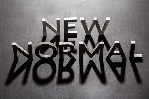 new normal word composed of silver metal letters on a flat matt black surface with shadows backlit.