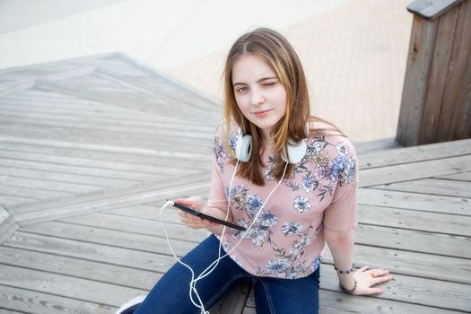 A young girl of 20 years old Caucasian appearance enjoys the sun and weather while sitting on a wooden podium in the park on a summer day.The girl is dressed in a floral T-shirt and jeans