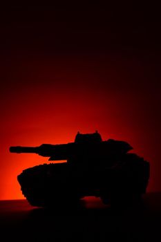 A military tank silhouette over a sunset background with deep red and orange hues which add atmospheric mood.