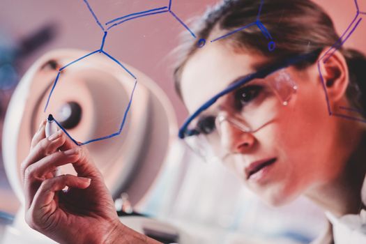 Portrait of a confident female health care professional in his working environment writing structural chemical formula on a glass board.