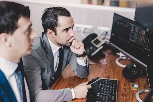 Businessmen trading stocks online. Stock brokers looking at graphs, indexes and numbers on multiple computer screens. Colleagues in discussion in traders office. Business success concept.