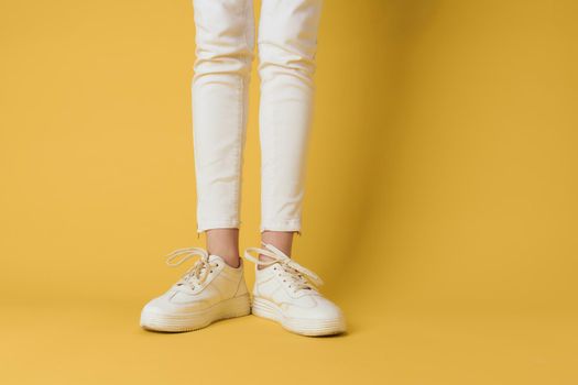 Female feet white sneakers attractive look fashion yellow background. High quality photo